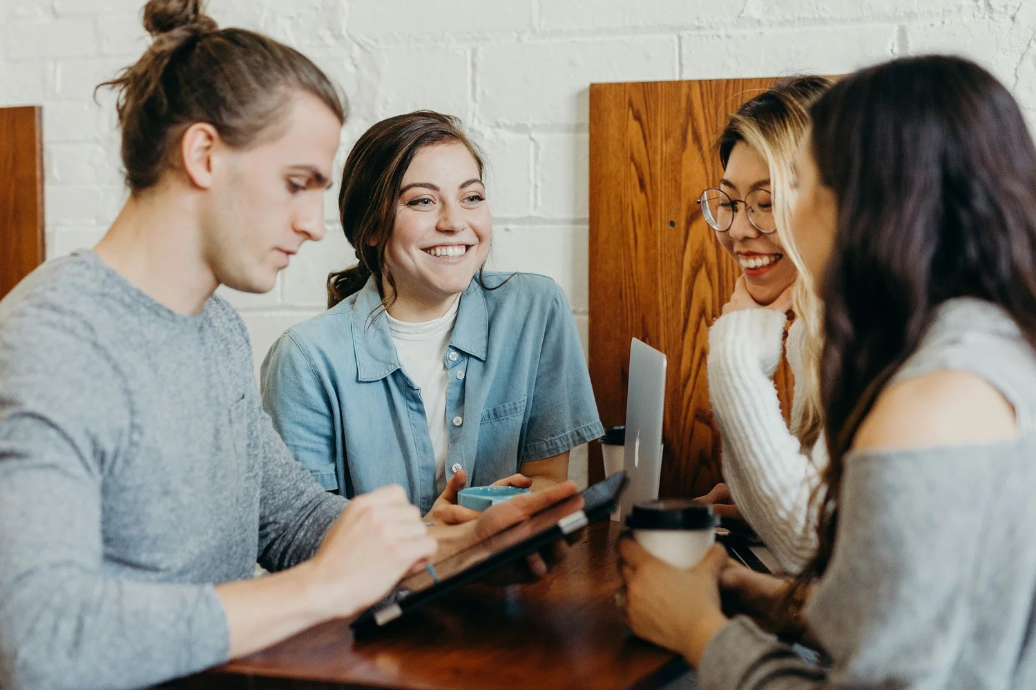 Four colleagues laughing around a cafe table with laptops